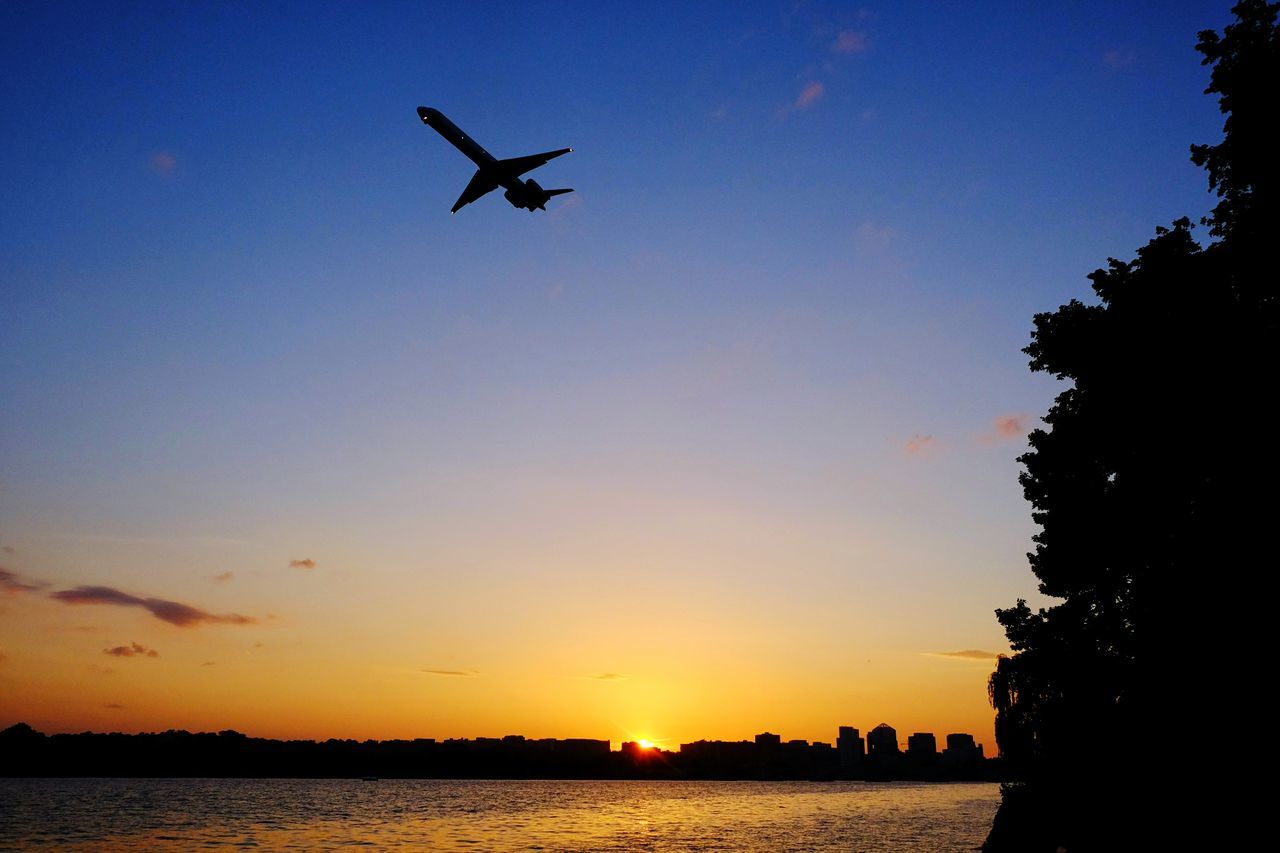 flying, clear sky, sunset, silhouette, water, waterfront, mid-air, blue, sun, copy space, sky, scenics, transportation, sea, nature, beauty in nature, mode of transport, tranquil scene, river, tranquility