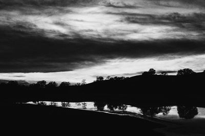 Silhouette trees by lake against sky