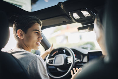 Young man asking questions about driving to mother while sitting in car