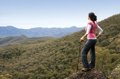 Full length of woman holding stick while standing on mountain against sky