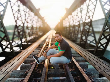 Side view portrait of man sitting on railway bridge during sunset