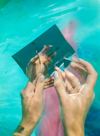 Cropped hands of woman holding mirror and prism in swimming pool
