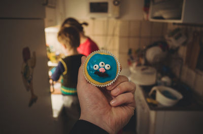 Cropped hand holding blue cupcake at kitchen