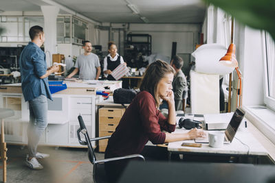 Creative businesswoman using laptop at desk while colleagues working in background