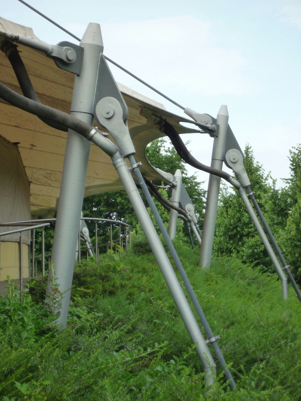 built structure, grass, architecture, sky, metal, low angle view, fence, field, connection, metallic, tree, plant, day, growth, no people, outdoors, railing, building exterior, old, bridge - man made structure