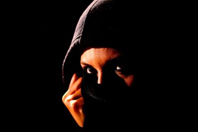 Close-up of woman covering face against black background