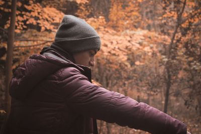 Side view of man standing by trees in forest during autumn