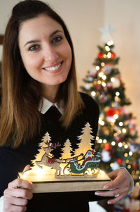 Portrait of young woman holding christmas tree at home