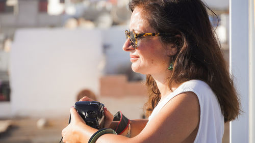 Woman holding camera standing in sunlight