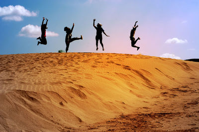 Silhouette people jumping on desert against sky