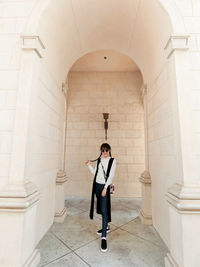 Full length portrait of smiling woman standing in corridor