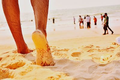 Low section of man walking on sand at beach