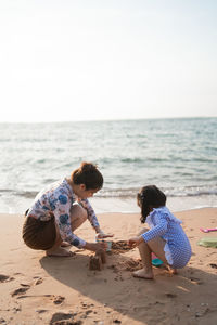 Rear view of mother and daughter at beach against sky