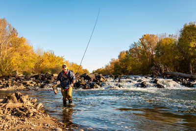 Man wearing cap fishing in river against sky