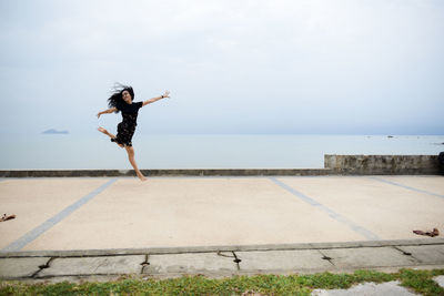 Full length of woman jumping against sea and sky