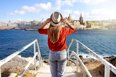 Beautiful girl enjoying view of valletta cityscape with the blue water of mediterranean sea