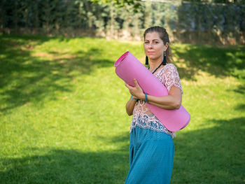 Young woman holding exercise mat while walking on grassy field
