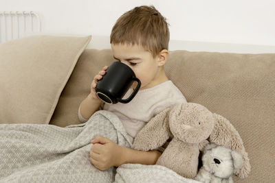 Sick little boy drinking hot tea on the bed at home. unwell, illness child wrapped in a blanket