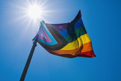 Low angle view of progress pride flag against blue sky