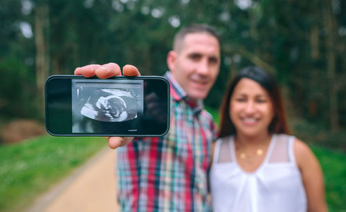 Man showing ultrasound scan of baby on mobile next to female pregnant