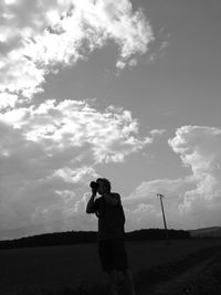 Woman standing on field against cloudy sky
