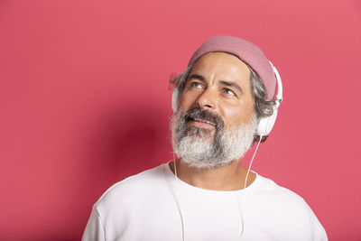 Cheerful grey-haired bearded man in casual pink hat and pullover posing isolated on fuchsia wall 