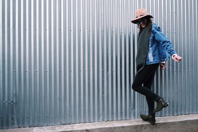 Full length of young woman standing by corrugated iron