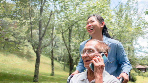 Smiling senior man talking on phone while granddaughter holding wheelchair