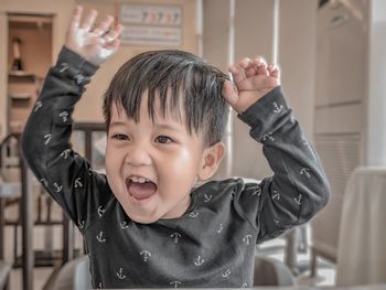 Close-up of cute boy with arms raised sitting at home