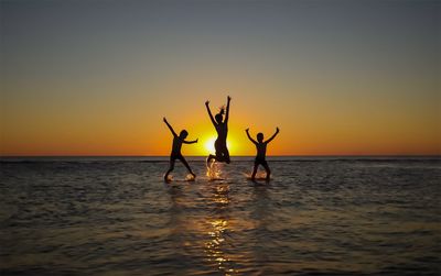 Silhouette people standing in sea against sky during sunset