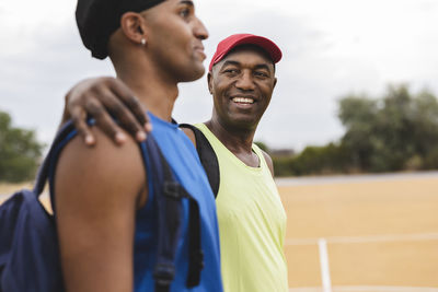 Smiling man with arm around son at basketball court