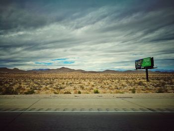 Road sign on countryside landscape against cloudy sky