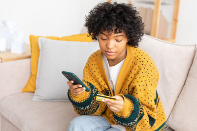 Young woman using mobile phone while sitting on sofa at home