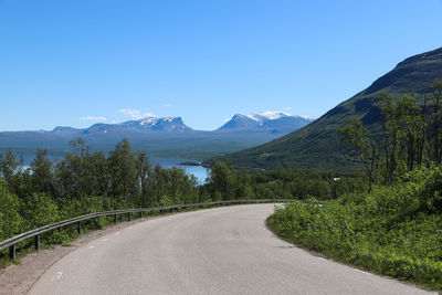 Road leading towards mountains against blue sky