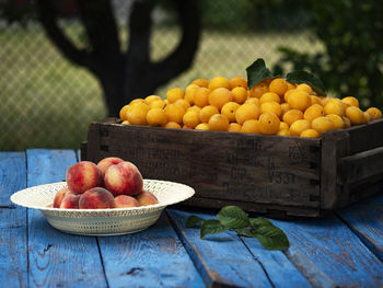 Organic cherry plums in vintage box and bowl with peaches on weathered blue wooden surface