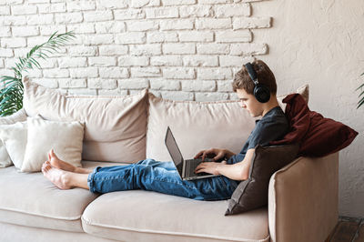 Rear view of woman using laptop while sitting on sofa at home