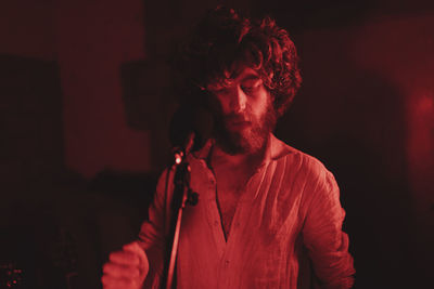 Trendy man singing with a rock band in red light at studio