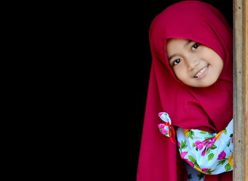 Portrait of smiling girl standing against black background