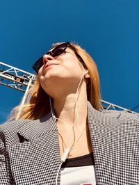 Low angle view of young woman listening to music against clear sky