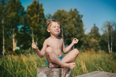 Little boy doing yoga sitting on stub. summer nature on background