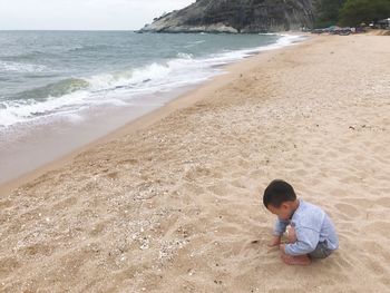 High angle view of boy crouching on sand at beach