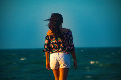 Rear view of woman standing in sea against sky