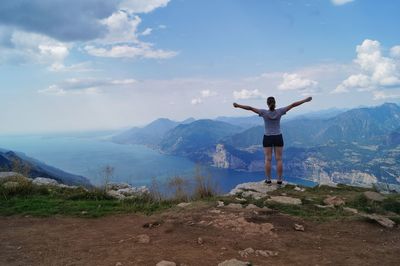 Rear view of woman with arms outstretched standing on mountain against sky