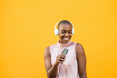 Smiling young woman holding camera while standing against yellow background