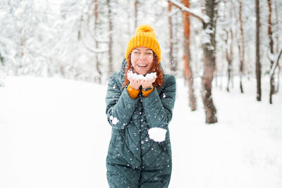 Cheerful girl in warm clothes playing with snow outdoors near the beautiful forest