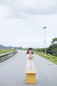 Woman with umbrella on road against sky