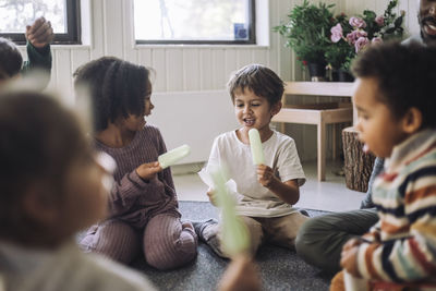 Boy and girl holding popsicle stick while sitting in classroom at kindergarten