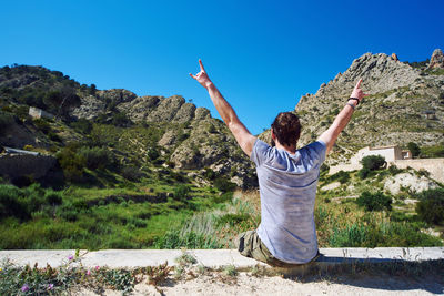 Rear view of man with arms raised against clear sky