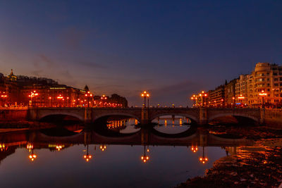 Illuminated bridge over river in city at night