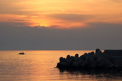 Silhouette rocks on sea against sky during sunset